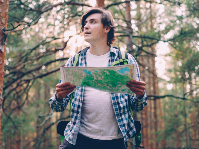 young man holding a map in the forest