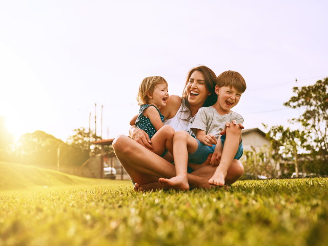 mother and children playing and laughing in a grassy yard