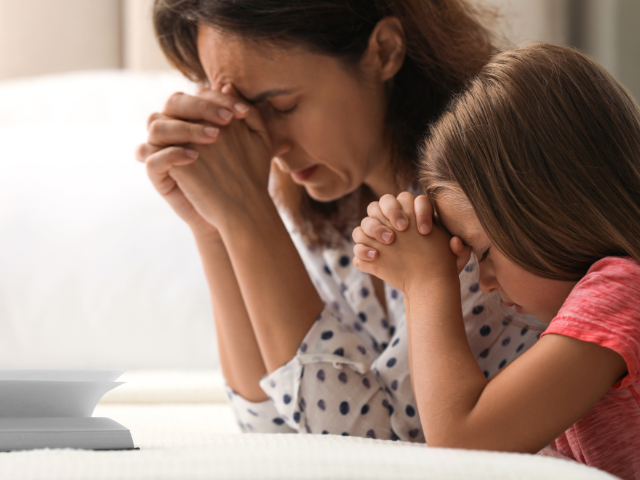 a mother and young daughter kneeling in prayer on a bedside