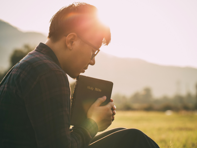 man praying with Bible in hand with a mountain in the background