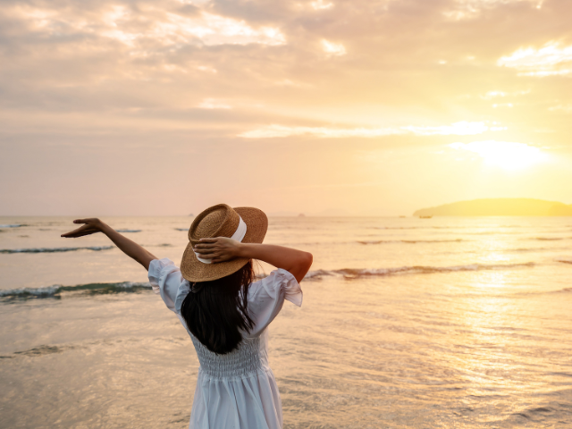 woman praising God as the sun rises over the ocean shore