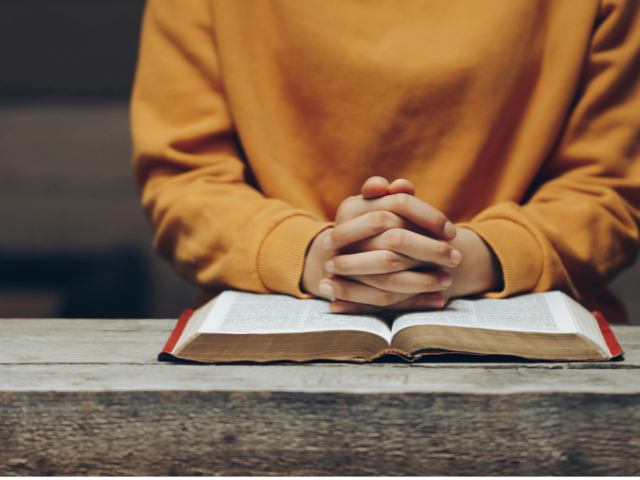 open Bible on a wood table with a young person