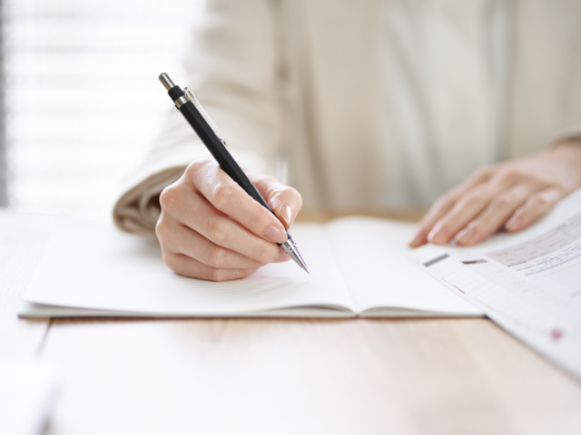 person writing in a notebook with a pen