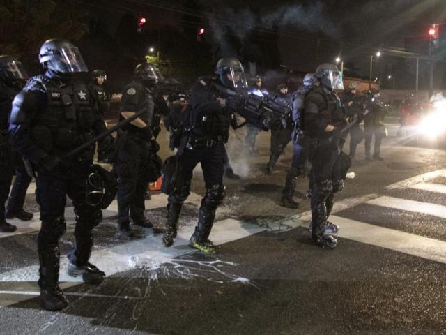 Portland police officers face demonstrators on 100th consecutive day of protests. (AP Photo/Paula Bronstein)