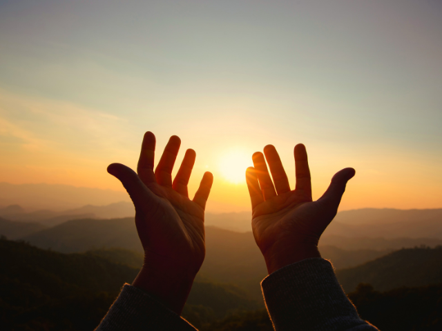 hands raised in praise with the setting sun in the background