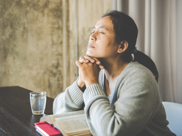 woman praying with her Bible open on the table