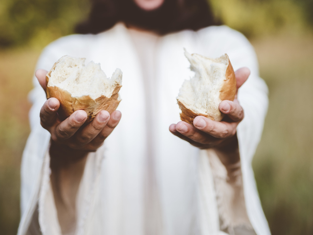 robed man holding out two halves of bread