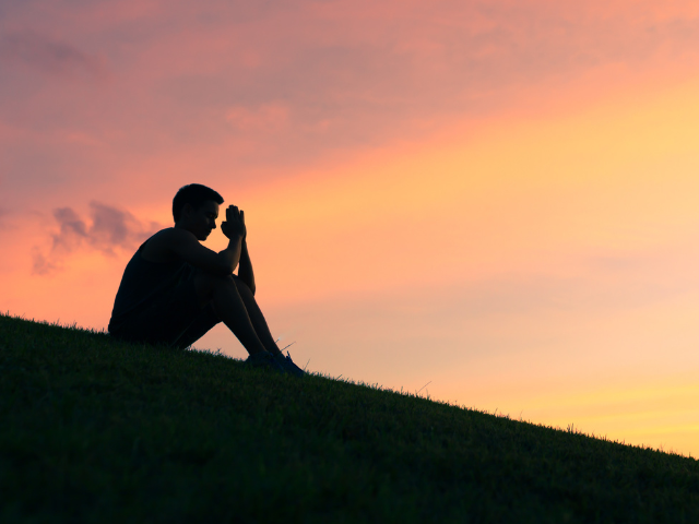 man sitting on a hillside at dusk praying
