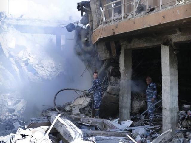 Firefighters stand in smoke that rises from the damage of the Syrian Scientific Research Center which was attacked by U.S., British and French military strikes to punish President Bashar Assad for suspected chemical attack against civilians.