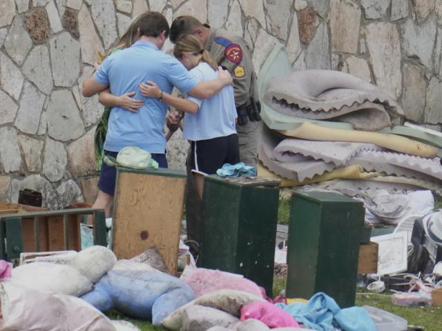 An officer prays with a family as they pick up items at Camp Mystic in Hunt, Texas on Wednesday, July 9, 2025. (AP Photo/Ashley Landis)