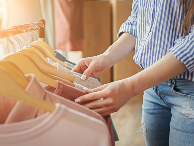woman choosing a shirt from hanging shirts in a closet