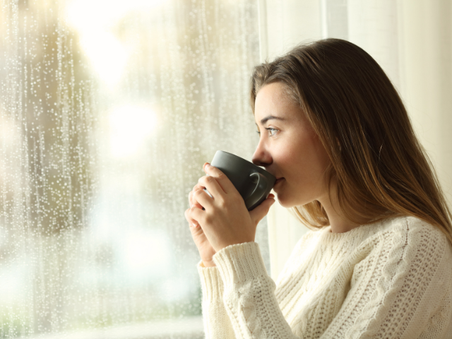 young woman looking out window while sipping a hot drink