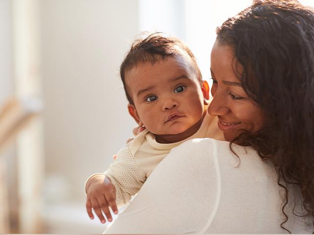 mom smiling and holding a baby up on her shoulder