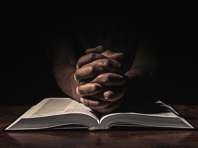 praying hands on top of an open Bible