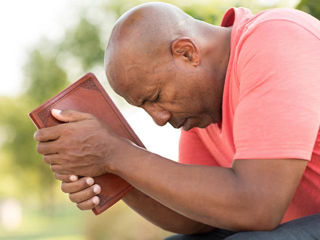 man praying outside with a Bible in his hands