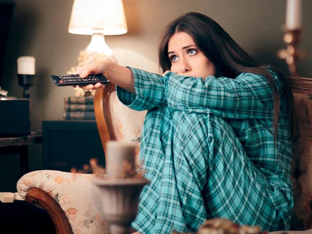 woman watching tv on a couch in her pajamas