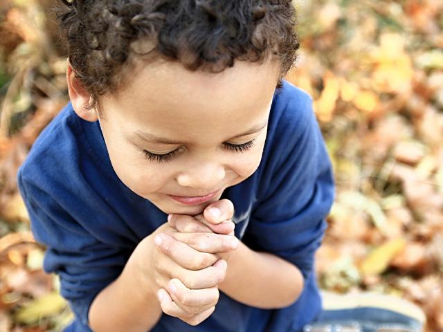 a little boy praying sitting down outside