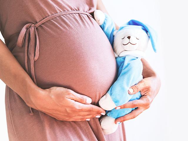 pregnant woman holding a teddy bear next to her belly