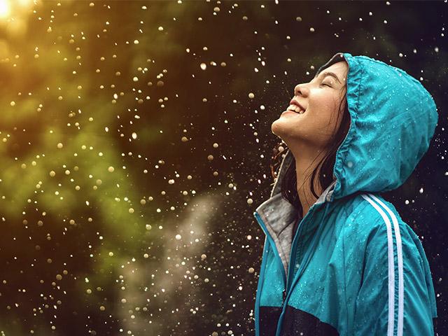 young woman wearing raincoat and smiling in the rain