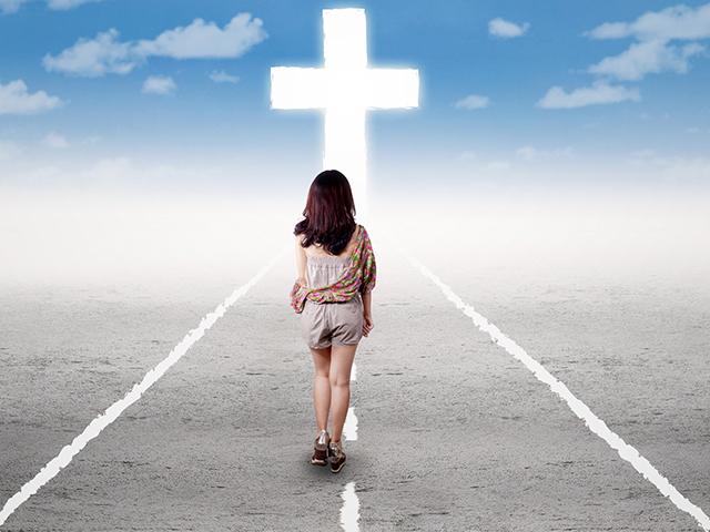 woman walking on the road toward the cross