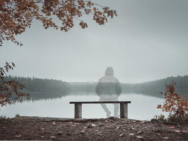 transparent man sitting on a bench by a lake