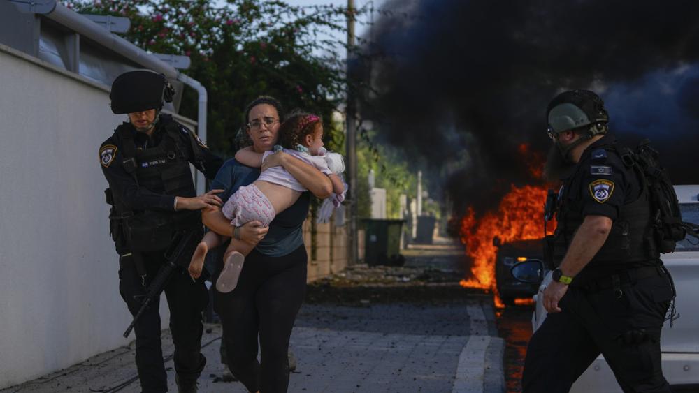 Police officers evacuate a woman and a child from a site hit by a rocket fired from the Gaza Strip, in Ashkelon, southern Israel, Saturday, Oct. 7, 2023. The rockets were fired as Hamas announced a new operation against Israel. (AP Photo/Tsafrir Abayov)