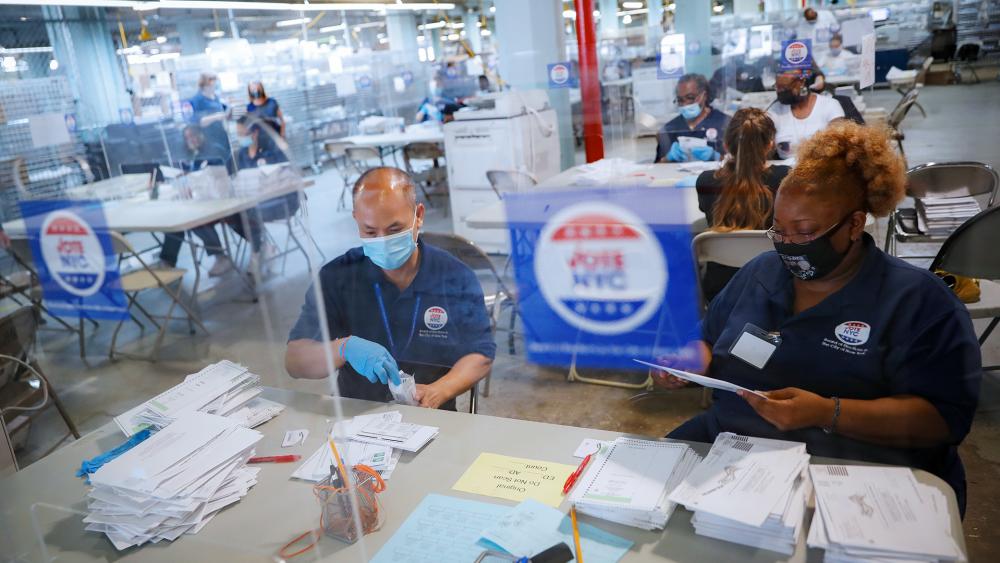 Workers wear personal protective equipment and are separated in pairs from fellow employees by plastic shields as they process ballots at a Board of Elections facility, Wednesday, July 22, 2020, in New York. (AP Photo/John Minchillo)