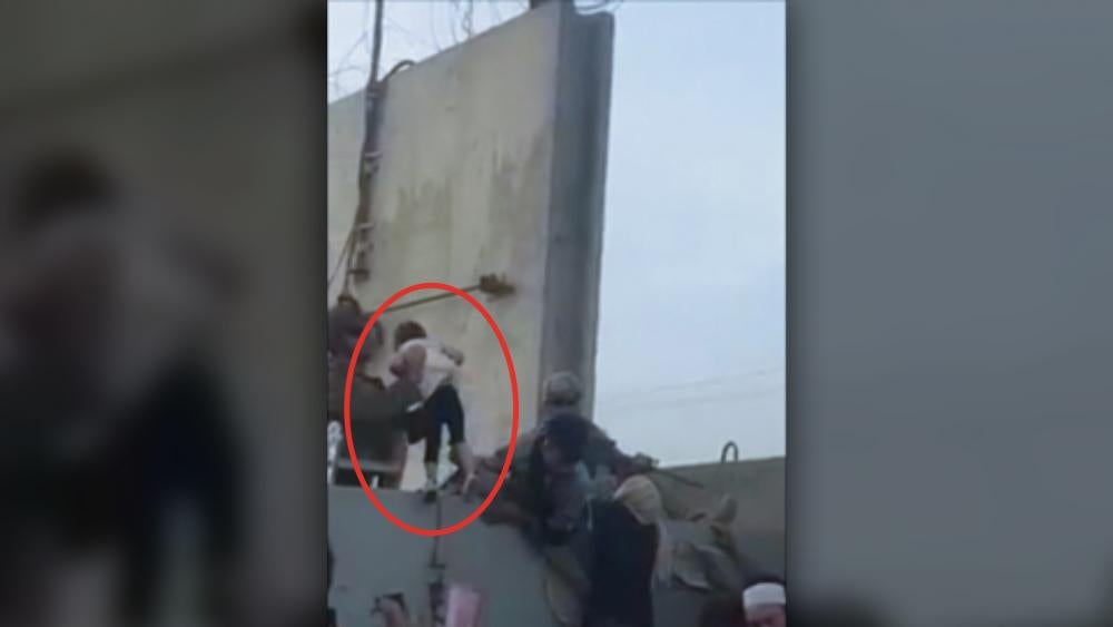 A desperate family hands their toddler over the fence at Kabul airport (Image: Screen shot from &quot;Rise to Peace&quot; video)
