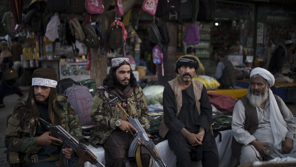 Taliban fighters sit next to street vendors at a local market in Kabul, Afghanistan