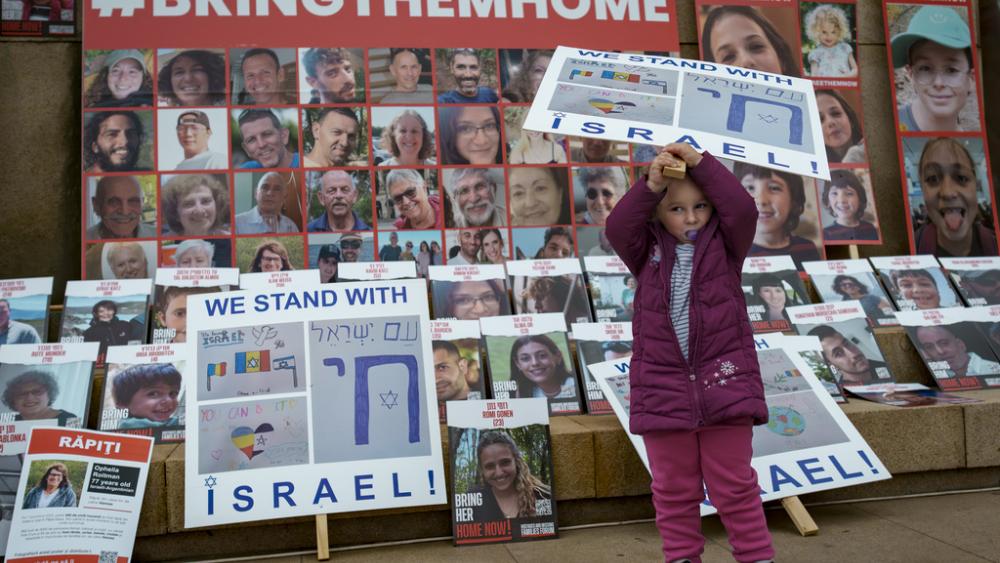 A child holds a banner backdropped by photographs of Israelis kidnapped by Hamas during a rally  in Bucharest, Romania, Thursday, Nov. 2, 2023. (AP Photo/Vadim Ghirda)