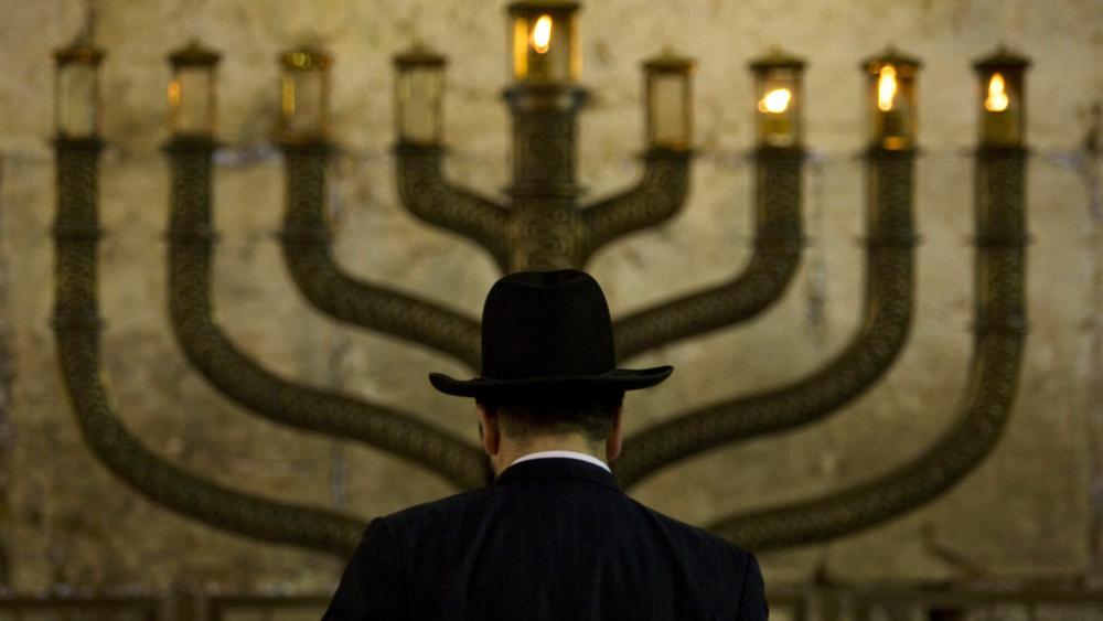 An Ultra-Orthodox Jewish man stands in front of a menorah on the third eve of Hanukkah, at the Western Wall, Judaism&#039;s holiest site in Jerusalem&#039;s old city, Sunday, Dec. 13, 2009.  (AP Photo/Sebastian Scheiner, File)
