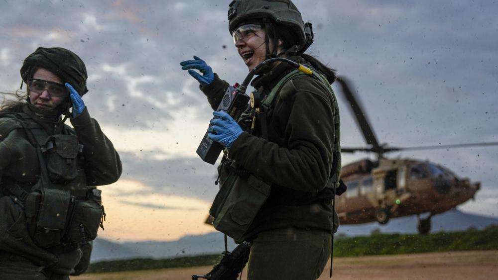 Israeli female paramedic soldiers take cover from the wind made by a landing military helicopter during an exercise simulating evacuation of wounded people in northern Israel, near the border with Lebanon, Tuesday, Feb. 20, 2024. (AP Photo/Ariel Schalit)