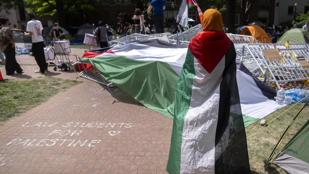 A person draped in the Palestinian flag stands at an encampment by students protesting against the Israel-Hamas war at George Washington University on Tuesday, April 30, 2024, in Washington. (AP Photo/Mark Schiefelbein)