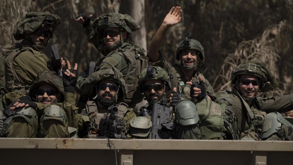 Israeli soldiers wave to the camera as they move on the back of a truck near the Israeli-Gaza border as seen from southern Israel, Monday, June 10, 2024. (AP Photo/Leo Correa)
