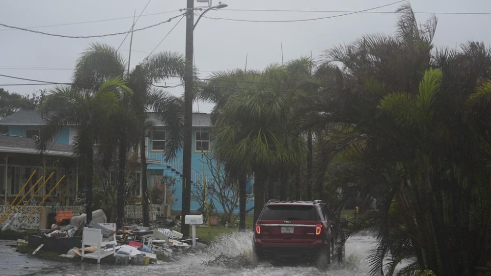 A car drives past a pile of debris from Hurricane Helene flooding, along a street that had already begun flooding from rain ahead of the arrival of Hurricane Milton, in Gulfport, Fla., Wednesday, Oct. 9, 2024. (AP Photo/Rebecca Blackwell)