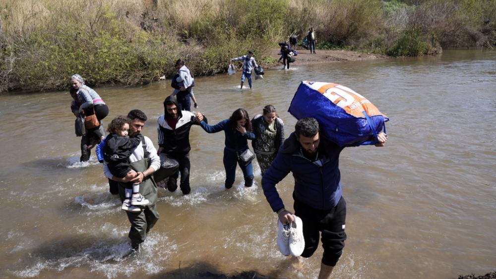 Syrian families who fled the clashes in Syria hold their luggages as they cross a river marking the border between Syria and northern Lebanon near the village of Heker al-Daher in Akkar province, Lebanon, Tuesday, March 11, 2025. (AP Photo/Hussein Malla)