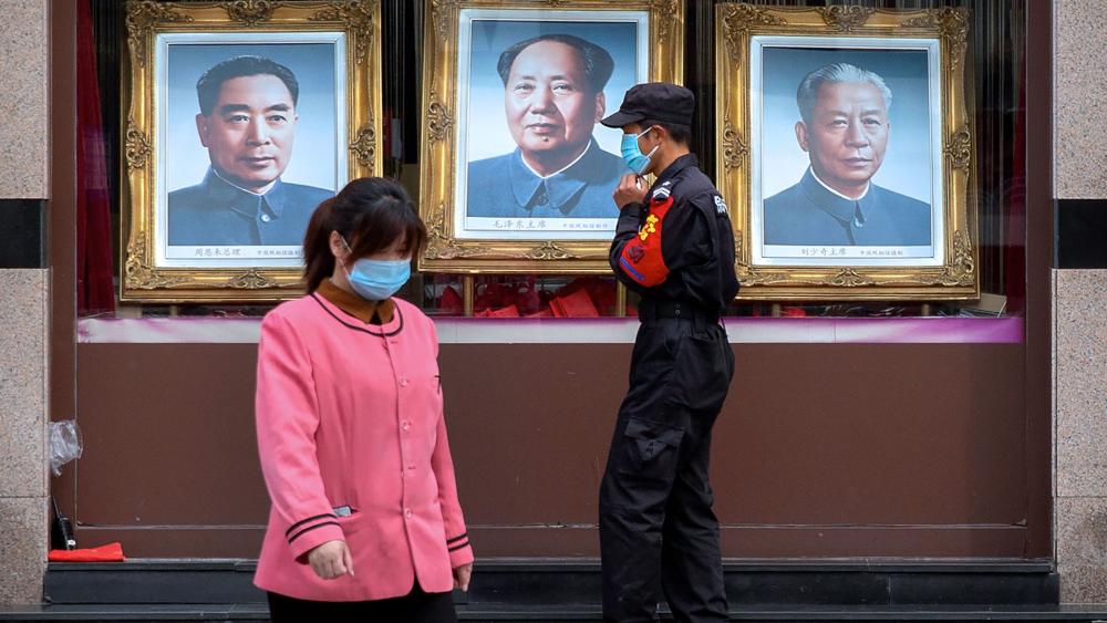 A security guard and worker walk past portraits of Chinese leaders, from left, Zhou Enlai, Mao Zedong, and Liu Shaoqi in the window of a photo studio in Beijing, April 15, 2020 (AP Photo/Mark Schiefelbein)