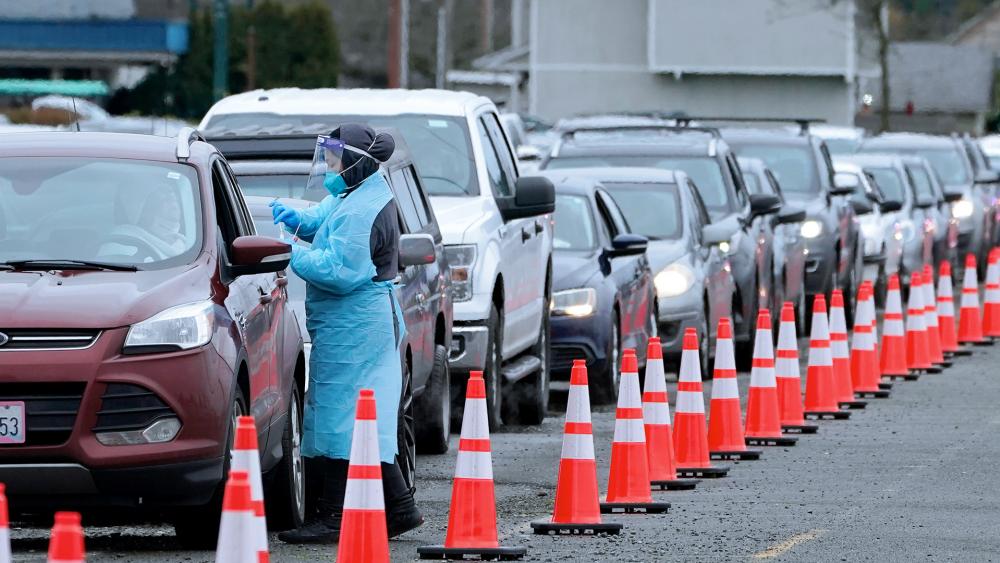 A worker at a drive-up COVID-19 testing clinic administers PCR coronavirus tests in Washington state as drivers wait several hours for testing. (AP Photo/Ted S. Warren)
