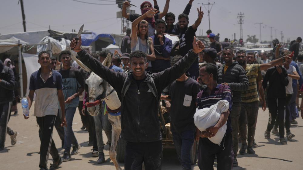 Palestinians wave while carrying bags of food and humanitarian aid packages from the Gaza Humanitarian Foundation, a U.S.-backed organization, in Rafah, southern Gaza Strip, June 9, 2025. (AP Photo/Abdel Kareem Hana)