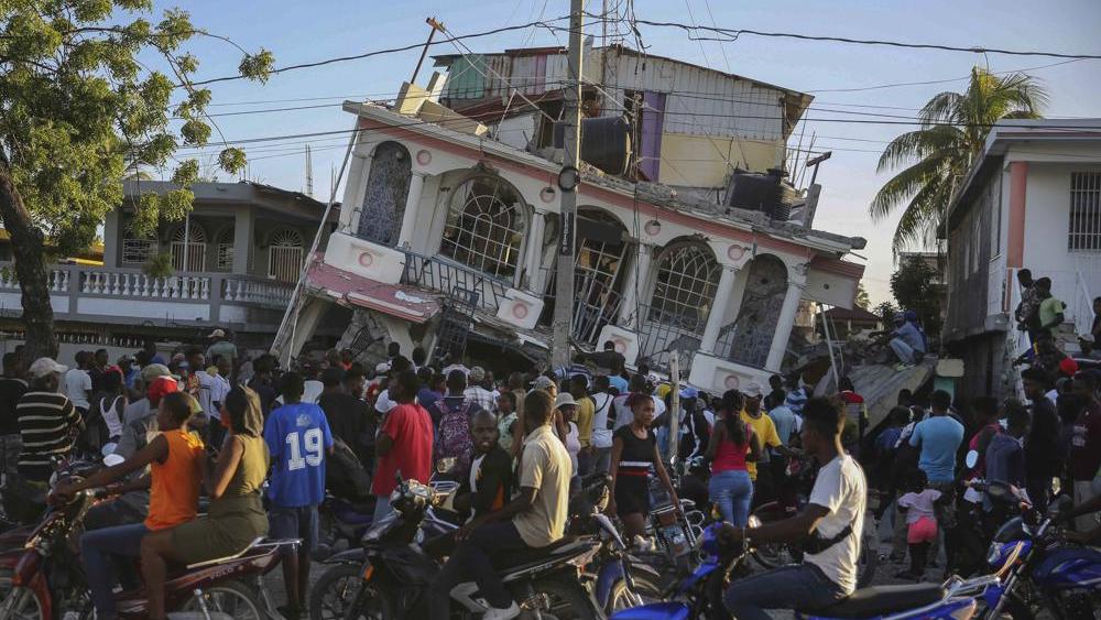 People gather outside the Petit Pas Hotel, destroyed by the earthquake in Les Cayes, Haiti, Saturday, Aug. 14, 2021. (AP Photo/Joseph Odelyn)