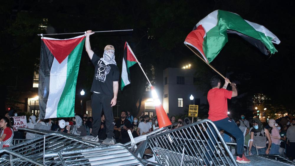George Washington University students, protest the Israel-Hamas war, stand on top of police barricades as they celebrate breaking through the fencing, in Washington, Monday, April 29, 2024. (AP Photo/Cliff Owen)