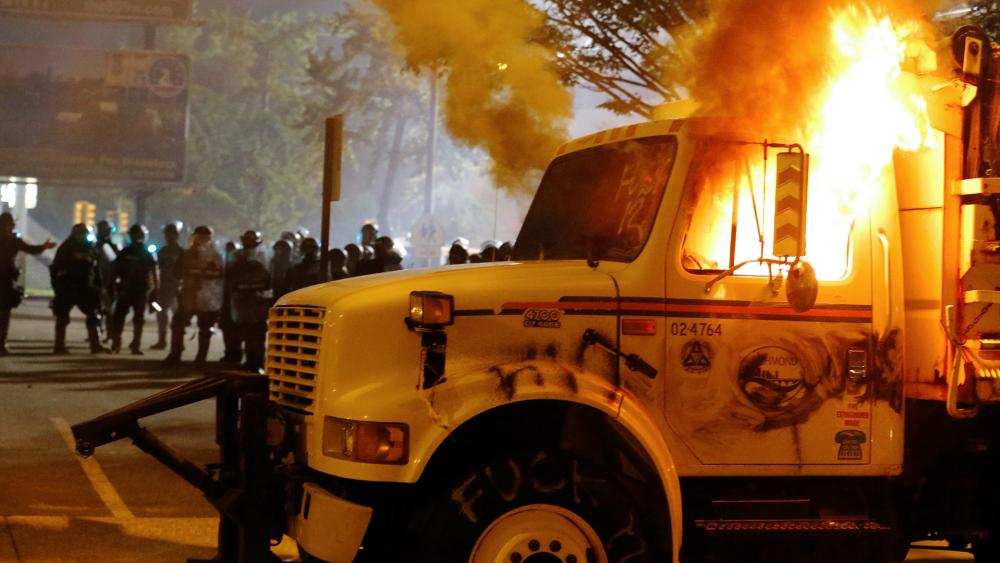Police stand in front of a utility vehicle that was set on fire by protesters during a demonstration outside the Richmond Police Department headquarters on Grace Street in Richmond, Va., July 25, 2020 (Joe Mahoney/Richmond Times-Dispatch via AP)