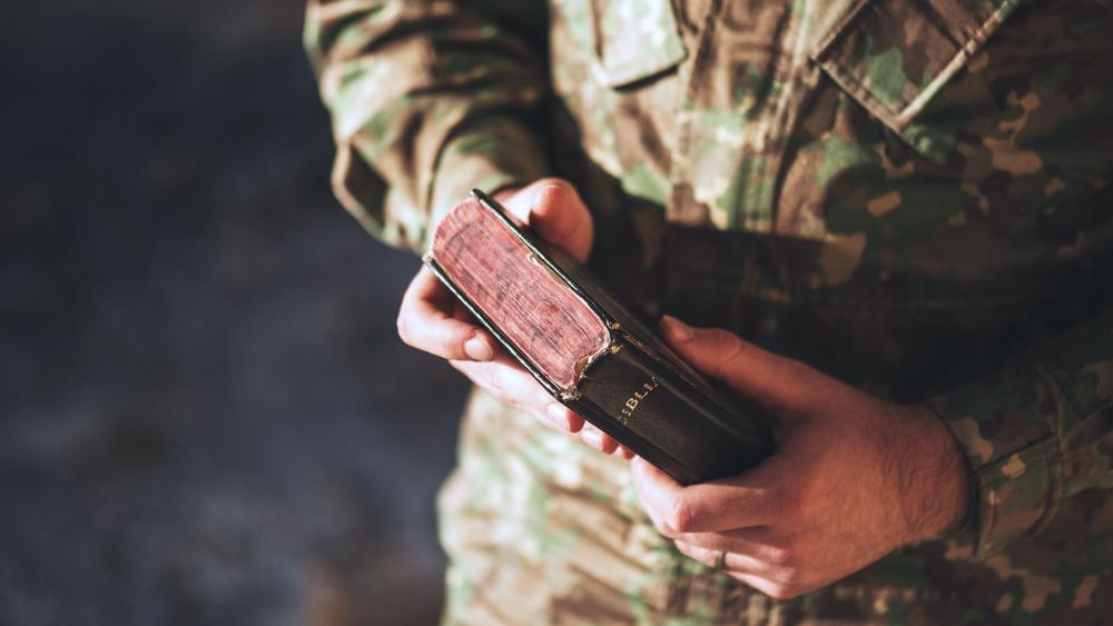 Soldier dressed in camouflage uniform holding a bible in his hand. (Adobe stock)
