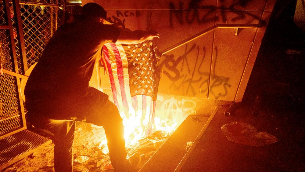 Protester burns an American flag outside the US Courthouse on July 20, 2020, in Portland, Ore. (AP Photo/Noah Berger)