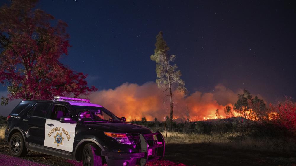 FILE - In this Sept. 28. 2020, file photo, a California Highway Patrol officer watches flames visible from the Zogg Fire near Igo, Calif. (AP Photo/Ethan Swope, File)