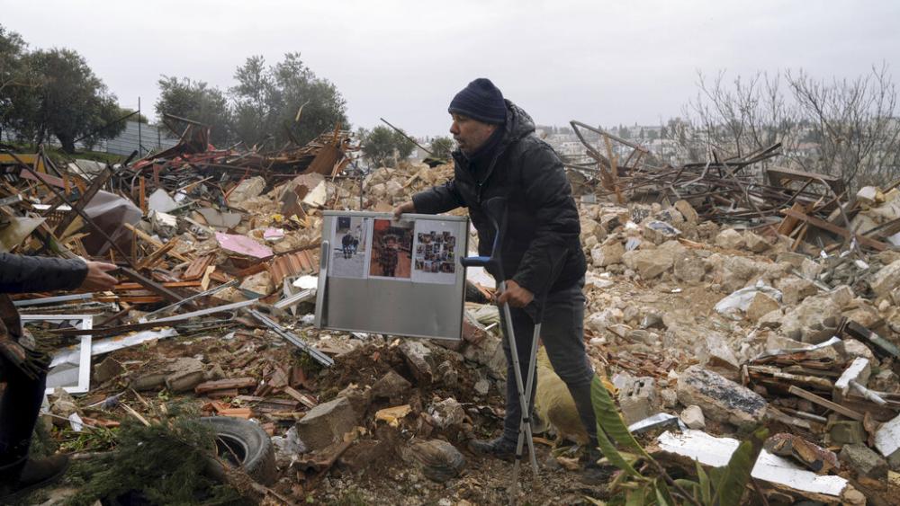 A Palestinian man carries family photos at the ruins of a house demolished by the Jerusalem municipality, in the flashpoint Jerusalem neighborhood of Sheikh Jarrah, Wednesday, Jan. 19, 2022. (AP Photo/Mahmoud Illean)