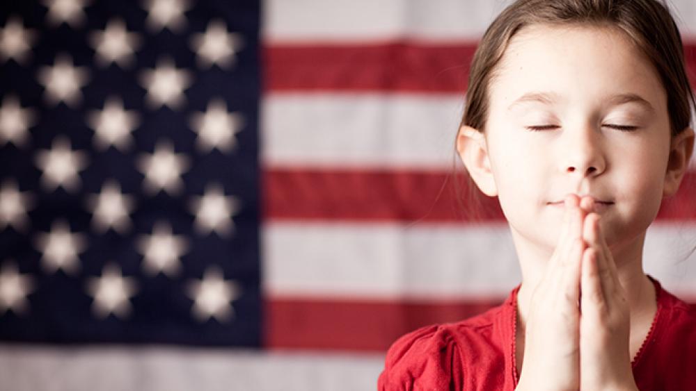 usa flag in the background and little girl praying with eyes closed